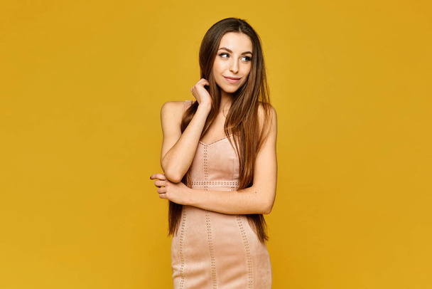 Young model woman with perfect slim body in a short beige dress on the yellow background, isolated with copy space - Fotó, kép