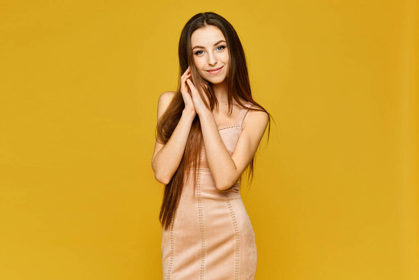 Young model woman with perfect slim body in a short beige dress on the yellow background - Photo, image