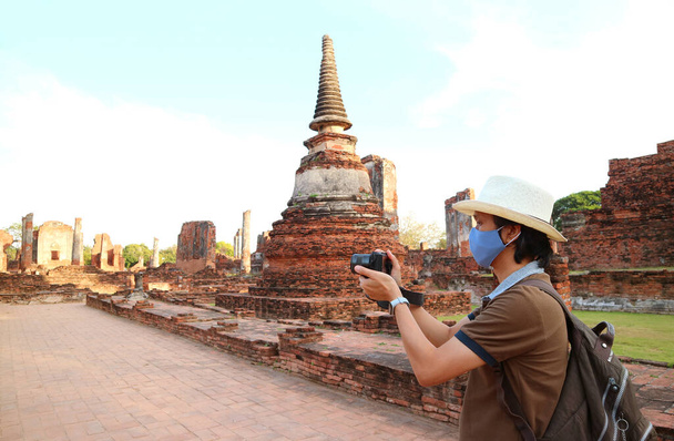 Путешественник в маске для лица фотографирует во время визита в храм Ват Пхра Си Санфан на фоне COVID-19, Аюттхая, Таиланд - Фото, изображение