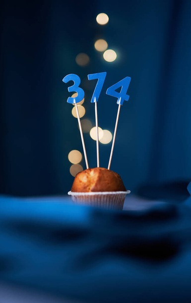 Cupcake di compleanno o muffin con il numero trecentosettantaquattro (374) e luci sullo sfondo blu. Concetto di compleanno o anniversario - Foto, immagini