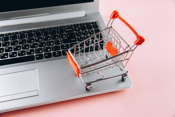 Black friday concept. Red trolley and laptop on pink background - Фото, изображение