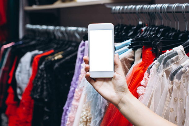 Female hand holding smartphone in clothes shop - Zdjęcie, obraz