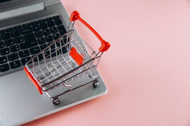 Black friday concept. Red trolley and laptop on pink background - Photo, Image