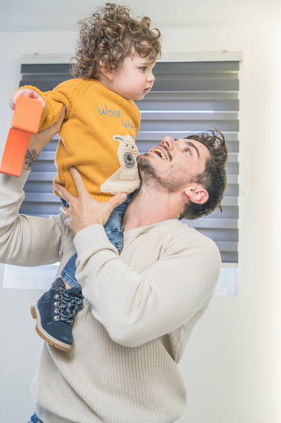Táta si hraje se svým synem se žlutým svetrem doma na podlaze a baví se - Fotografie, Obrázek