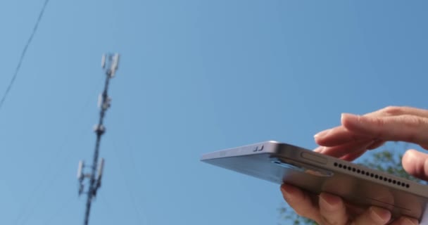 Een man werkt op een tablet, raakt het scherm met zijn vingers tegen de achtergrond van een mobiele communicatietoren, close-up.  - Video