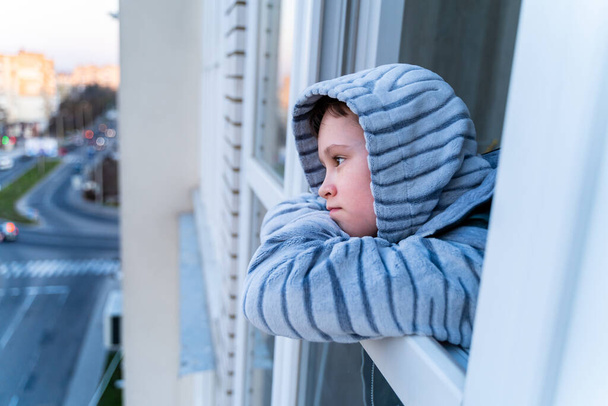 Little boy in gray pajamas looking through window. isolation at home. Stay at home quarantine coronavirus. COVID-2019 disease concept - Foto, Imagen