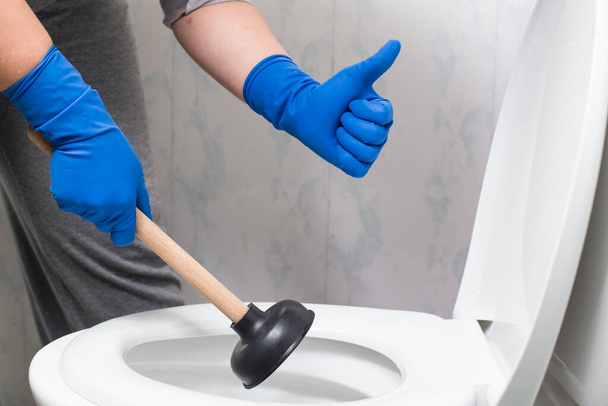 Hands in gloves holding suction cup and showing thumb up near by toilet bowl. - Фото, зображення