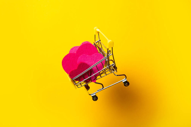 grocery cart with pink hearts flies on bright yellow background - Zdjęcie, obraz