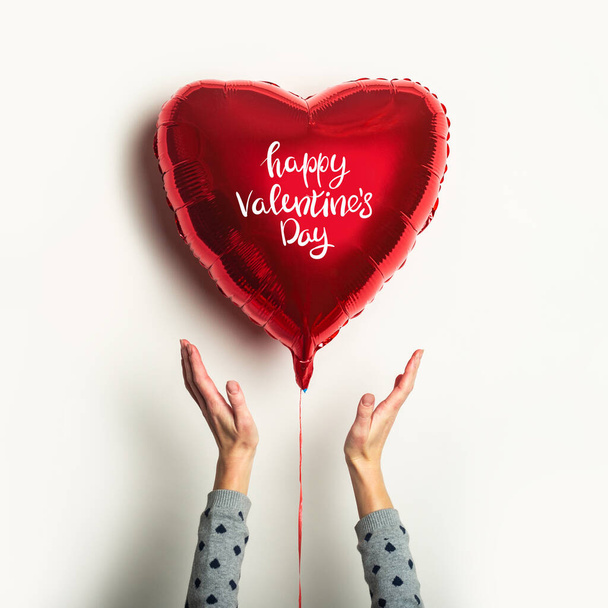 Frauenhände greifen nach dem Luftballon in Herzform mit der Aufschrift Happy Valentine 's Day auf weißem Hintergrund. - Foto, Bild