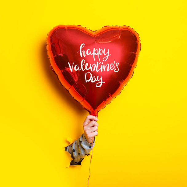 Ženská ruka drží nafukovací balón s nápisem Šťastný Valentýn na roztrhaném žlutém pozadí. - Fotografie, Obrázek