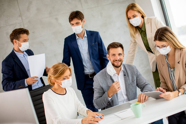 İş adamlarının bir toplantısı var ve ofiste çalışıyorlar. Koronavirüsten korunmak için maske takıyorlar. - Fotoğraf, Görsel