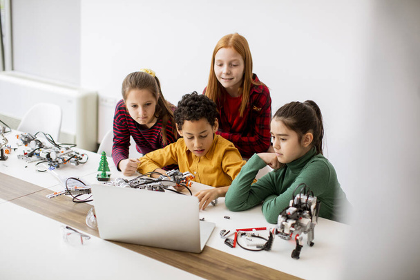 Groupe d'enfants heureux programmant des jouets électriques et des robots dans une salle de classe de robotique - Photo, image