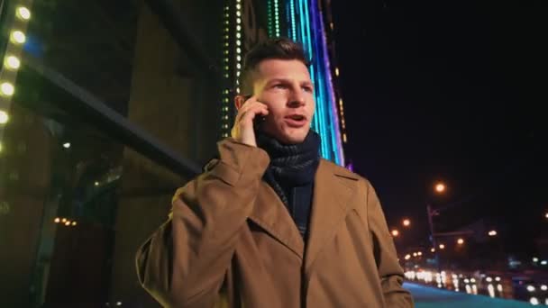 Hombre enojado hablando en el teléfono móvil fuera del centro comercial Glowing por la noche  - Imágenes, Vídeo