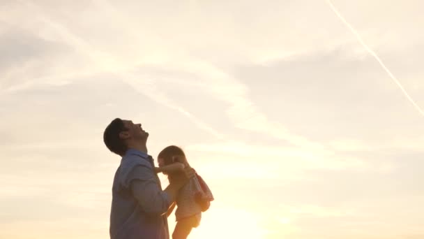 幸せな家族のお父さんと小さな娘が公園で遊んでいます。父は青い空に幸せな娘を投げ出す。父と子供の遊び、笑いと抱擁を一緒に。家族旅行だ。親の腕の中で赤ちゃん。お父さん休み - 映像、動画