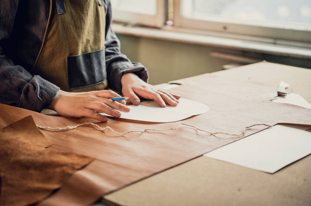 A young guy in a leather workshop transfers a pattern from paper to leather - Photo, image