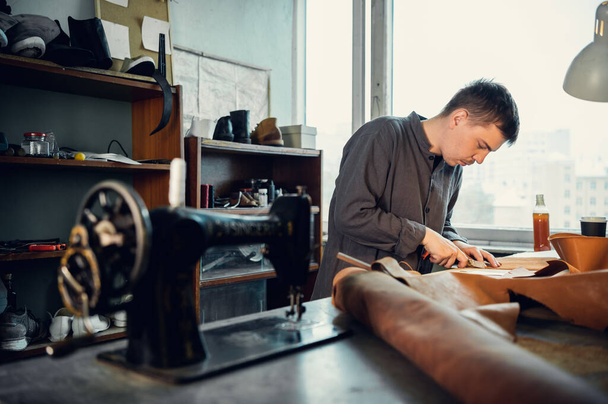 Mladý švec ve své dílně šije kůži na šicí stroj, vyrábí originální boty na objednávku - Fotografie, Obrázek