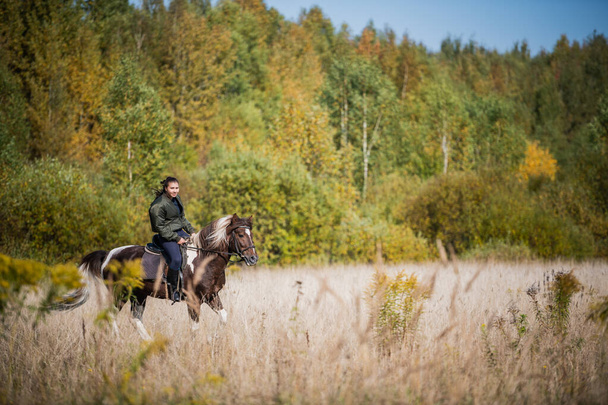 Μια ηλιόλουστη μέρα, το κορίτσι κάνει μια βόλτα με το άλογο μέσα από τις εκτάσεις της περιουσίας της. - Φωτογραφία, εικόνα