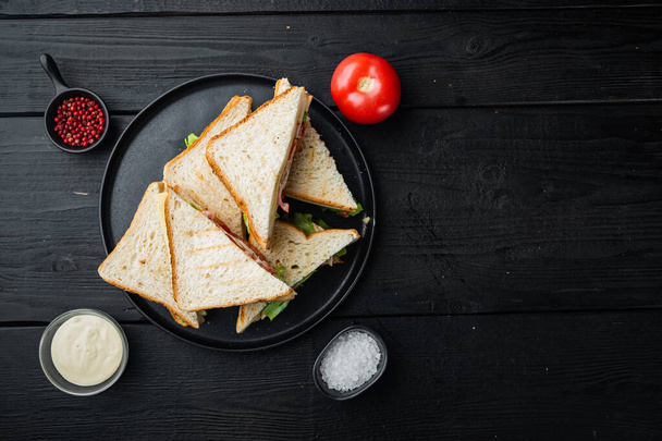 Sandwich with ham, cheese, tomatoe, lettuce, chicken meat and toasted bread, on black wooden background, top view with copy space for text - Photo, Image