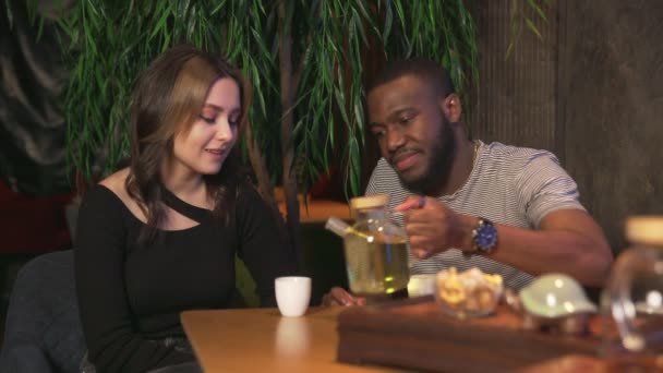 Couple multinational homme africain et femme caucasienne boit du thé chinois et mange des biscuits dans un café traditionnel - Séquence, vidéo