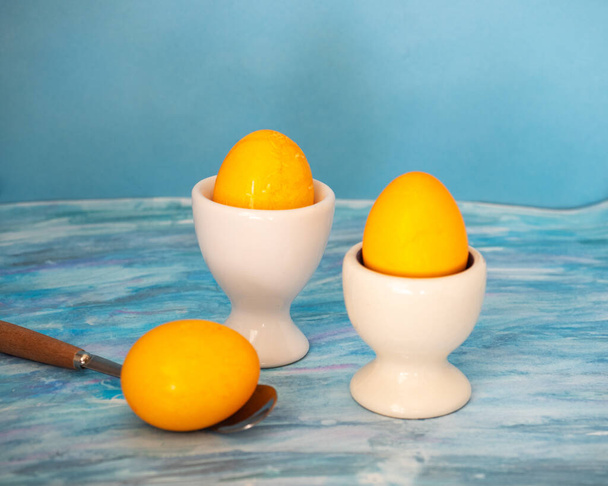 Desayuno de Pascua con huevos pintados de amarillo, huevo en un soporte y cuchara sobre un fondo azul - Foto, imagen