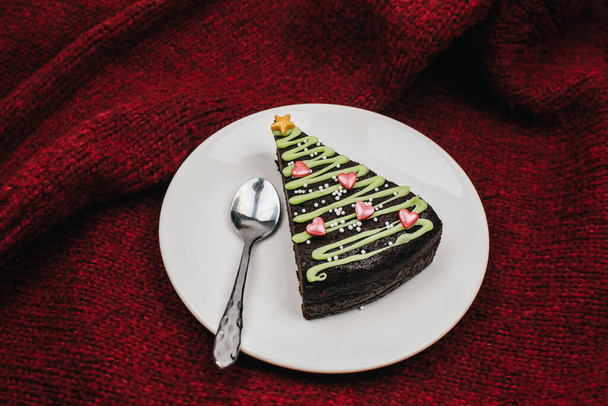 Ein Stück süßer Schokoladenkuchen für Heiligabend in Form von Weihnachtsbäumen mit grünem Zuckerguss und festlichen Streusel auf weißem Teller. Süßes hausgemachtes Weihnachts- oder Wintergebäck. - Foto, Bild