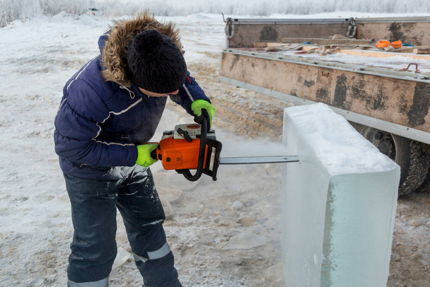 Εγκατάσταση εργασίας με αλυσοπρίονο στα χέρια του κάτω από το κομμάτι πάγου - Φωτογραφία, εικόνα
