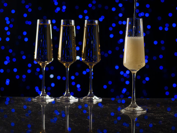Lange glazen glazen gevuld met mousserende wijn tegen een blauwe bokeh achtergrond. Een populaire alcoholische drank. - Foto, afbeelding