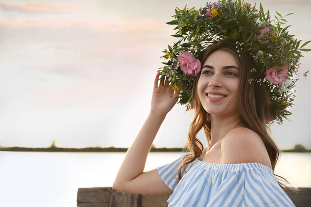 Young woman wearing wreath made of beautiful flowers near river - Foto, imagen