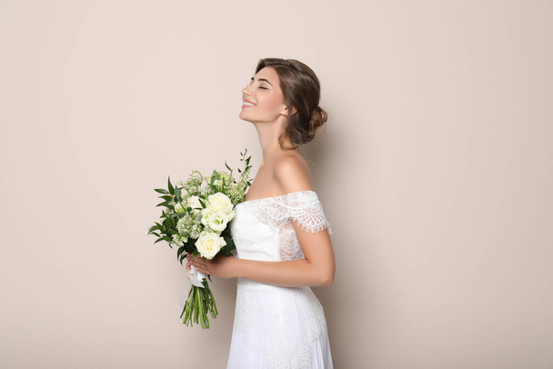 Young bride wearing wedding dress with beautiful bouquet on beige background - Photo, Image