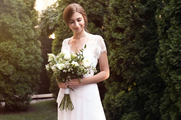 Gorgeous bride in beautiful wedding dress with bouquet outdoors - 写真・画像