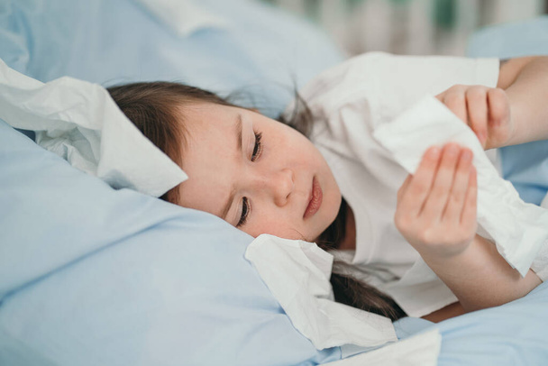 The little girl caught a cold. Children sneeze into a handkerchief. The child is ill and is being treated at home. Seasonal colds in children - Foto, Imagen