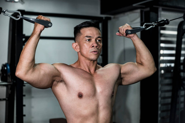 Un hombre asiático en forma hace unos rizos dobles de bíceps de cable en el gimnasio. Ejercicio del día del brazo - Foto, imagen