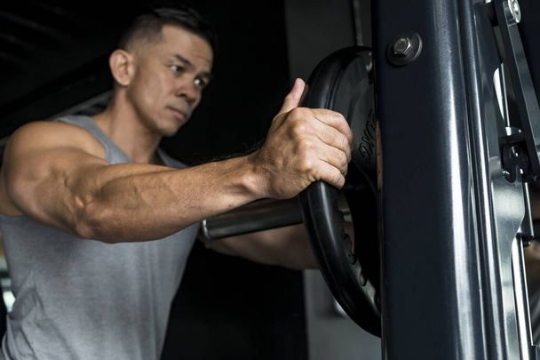 Mężczyzna dodaje gumowany talerz na maszynie kowalskiej na trening lub asystowanie klientowi na siłowni - Zdjęcie, obraz