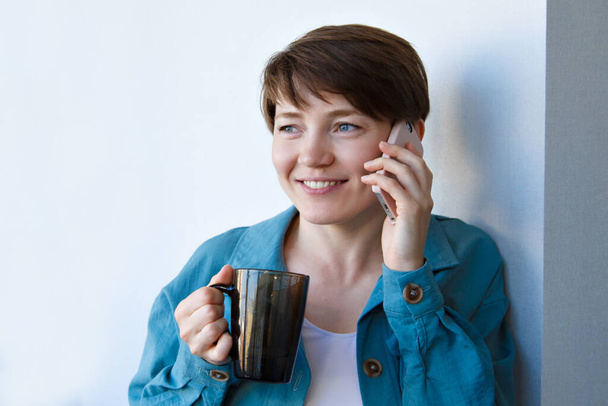 the concept of employment, interviews, advertising digital technology - woman drinking coffee and talking on the phone. Smiling woman with cup makes a call. Morning of girl - Фото, изображение