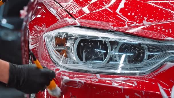 Автомойка - человек наносит чистящую пену на красный автомобиль щеткой - Кадры, видео