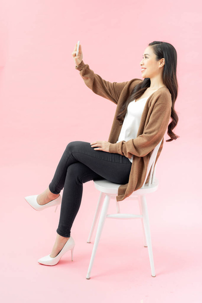 Full length πορτρέτο της πανέμορφης ευτυχισμένη γυναίκα στην επιχείρηση φορούν selfie λήψη στο κινητό τηλέφωνο, ενώ κάθεται στην καρέκλα - Φωτογραφία, εικόνα