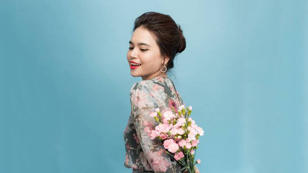 Adorable, beautiful woman holding bouquet of flowers isolated on blue background - 写真・画像