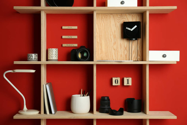 Stylish wooden shelves with photography equipment and decorative elements on red wall - Zdjęcie, obraz