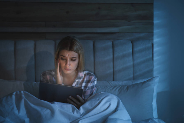 Young woman using tablet in bed at night. Sleeping disorder problem - Фото, изображение