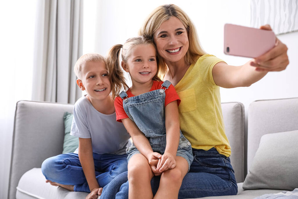 Happy mother taking selfie with her children on sofa at home - Фото, изображение
