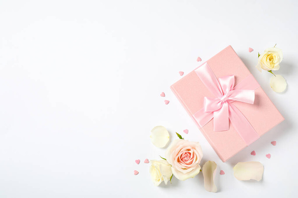 Pink gift box and beautiful flowers on white background, flat lay. Space for text - Foto, Bild
