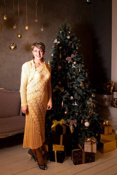 35-40 yaşlarında güzel bir kadının portresi. Bir Noel ağacının yanında sarı uzun bir elbise içinde.. - Fotoğraf, Görsel