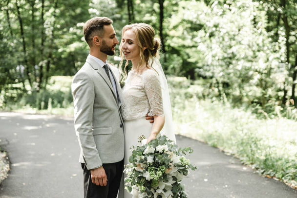 Lovely newlyweds hugging and smiling in a green park. Portrait of the bride and groom in a lace dress. Wedding day of a happy newlywed couple - Φωτογραφία, εικόνα