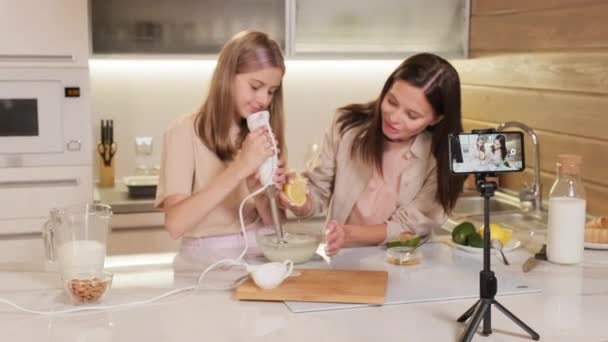 Medium beelden van lachende vrouw en haar mooie tienerdochter koken, het bereiden van mengsel voor zelfgemaakte ijs en filmen video recept op telefoon camera op statief - Video