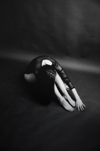 Stylish and fashionable photo, black and white art portrait of a girl in a bodysuit. The girl freely dances and moves in the Studio on a dark background, posing in front of the camera - Фото, зображення