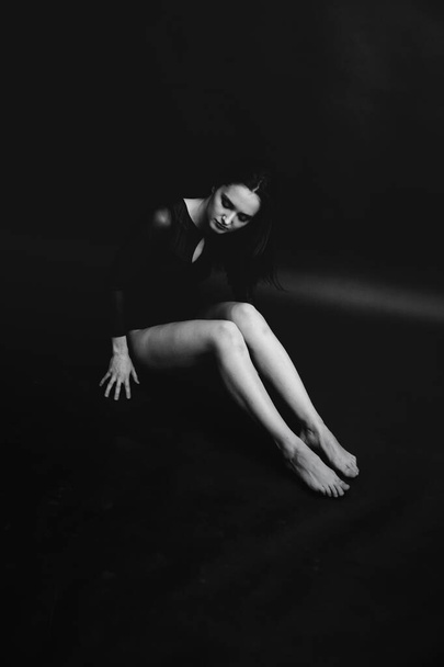 Stylish and fashionable photo, black and white art portrait of a girl in a bodysuit. The girl freely dances and moves in the Studio on a dark background, posing in front of the camera - Foto, immagini