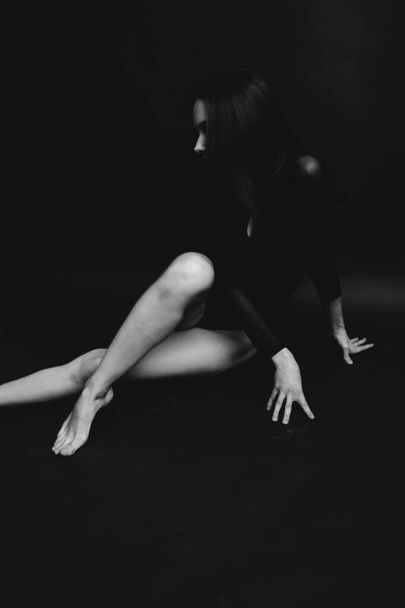Stylish and fashionable photo, black and white art portrait of a girl in a bodysuit. The girl freely dances and moves in the Studio on a dark background, posing in front of the camera - Photo, image