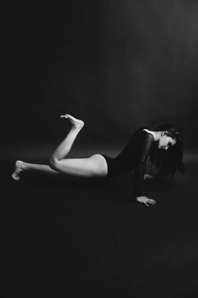 Stylish and fashionable photo, black and white art portrait of a girl in a bodysuit. The girl freely dances and moves in the Studio on a dark background, posing in front of the camera - Zdjęcie, obraz