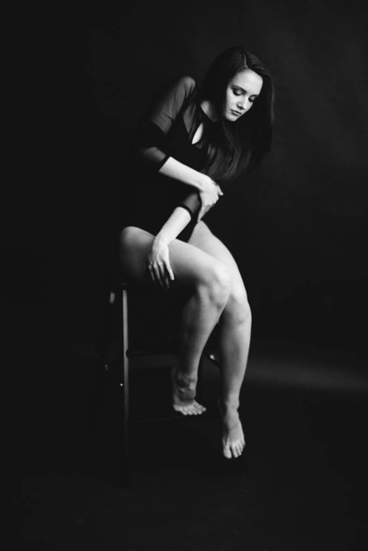 Stylish and fashionable photo, black and white art portrait of a girl in a bodysuit. The girl freely dances and moves in the Studio on a dark background, posing in front of the camera - Foto, imagen