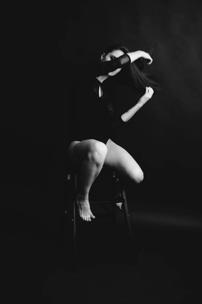 Stylish and fashionable photo, black and white art portrait of a girl in a bodysuit. The girl freely dances and moves in the Studio on a dark background, posing in front of the camera - Фото, изображение